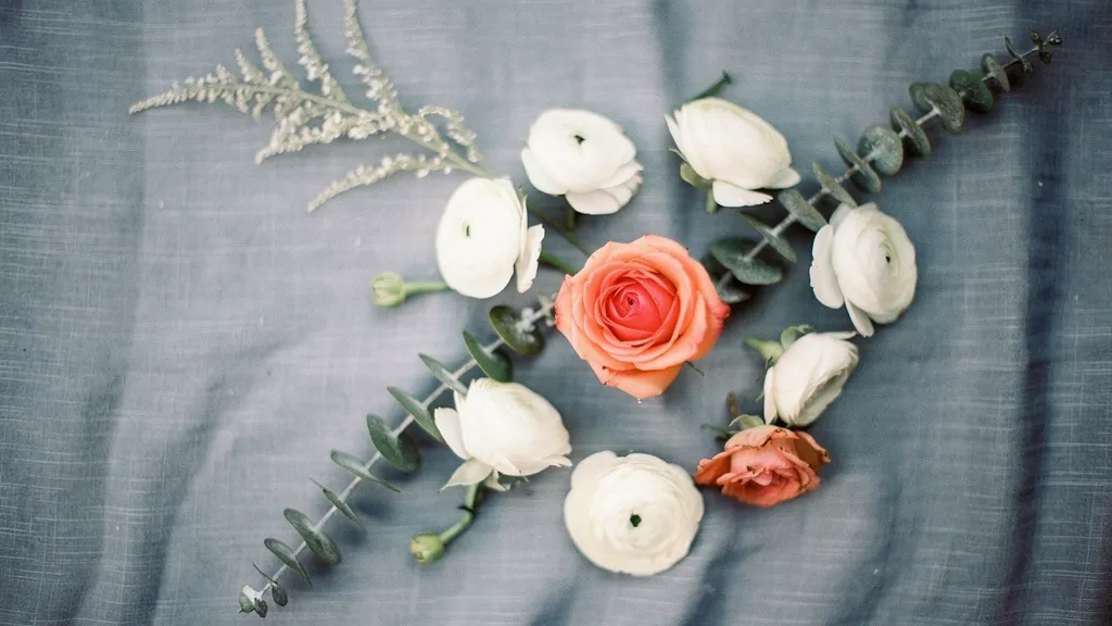 Coral blush roses, white ranunculus, and eucalyptus laid on a misty blue linen, creating a delicate floral arrangement.
