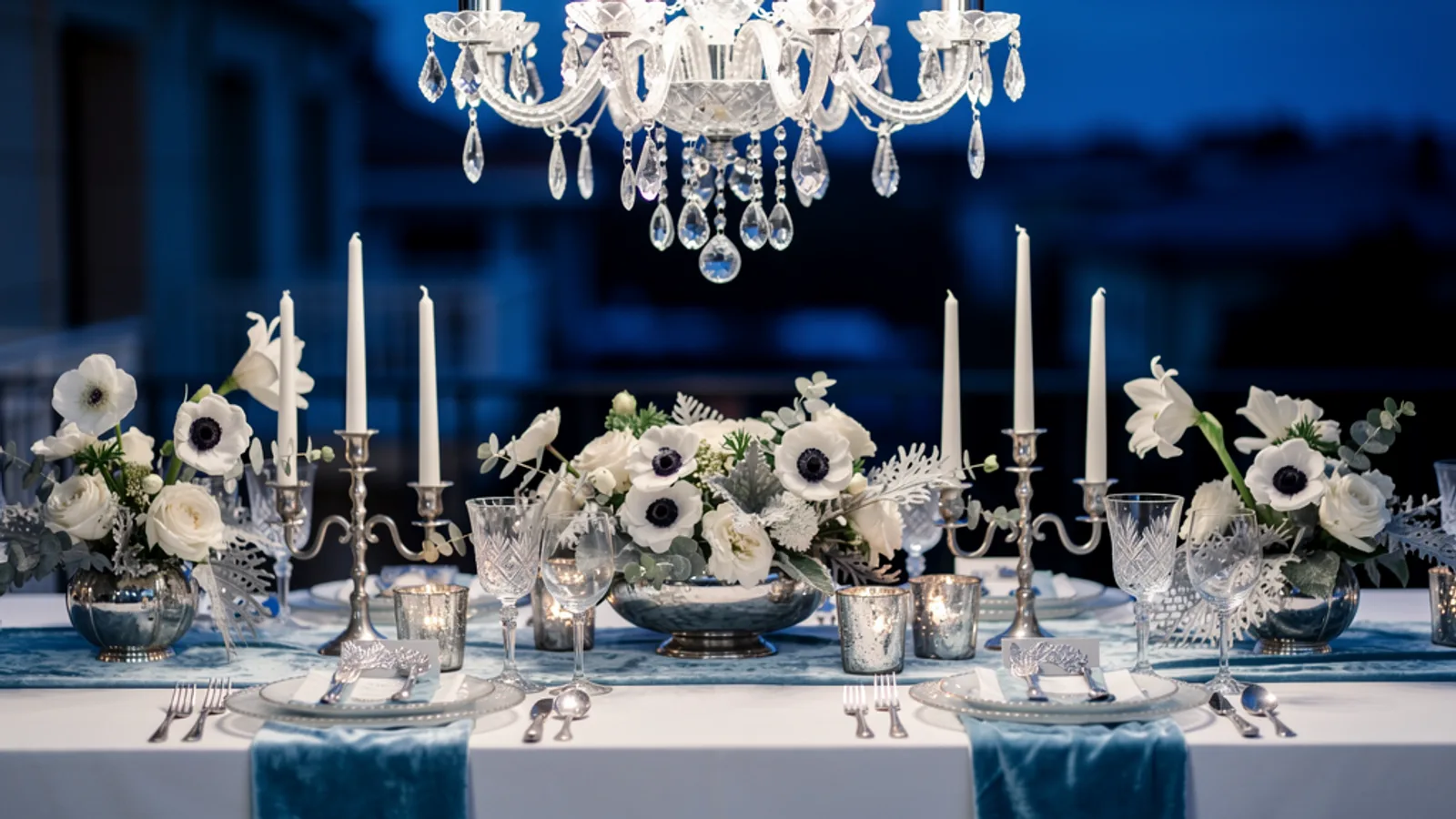Cool Blue Subzero wedding aesthetic — A beaded crystal chandelier over a frost-white tablescape at blue hour, light refracting into cold prisms.