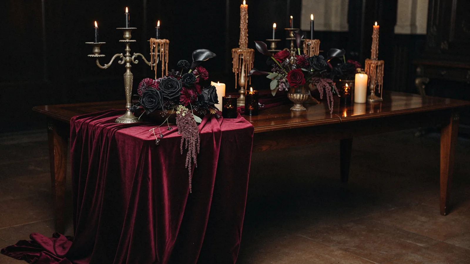 Dark Romantic Vamp wedding aesthetic — A long walnut table half-swallowed in shadow, dripping beeswax tapers in tarnished brass candelabra, merlot velvet runner pooling onto the floor.